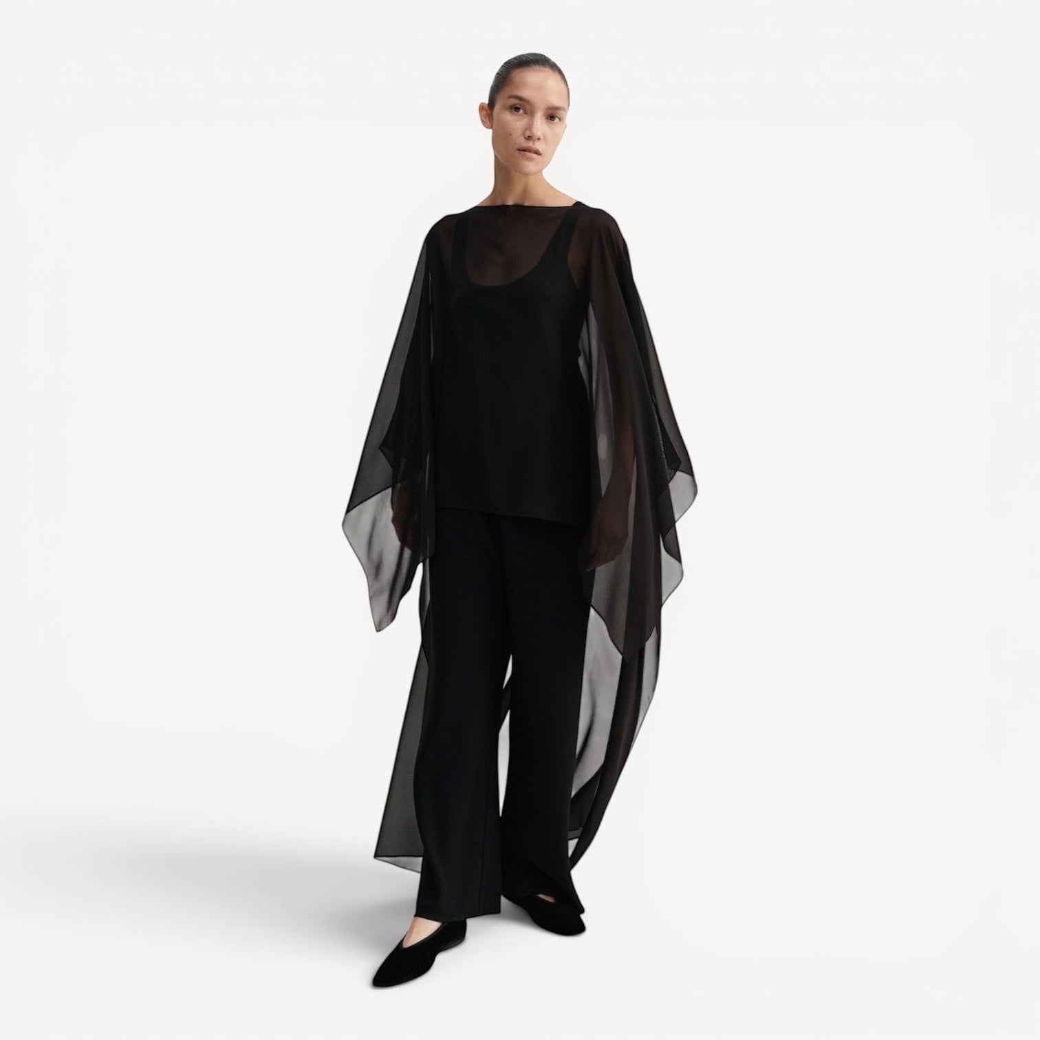 Lula Studio Prague black silk chiffon cape with asymmetric drape and boatneck, worn over black tank and trousers.