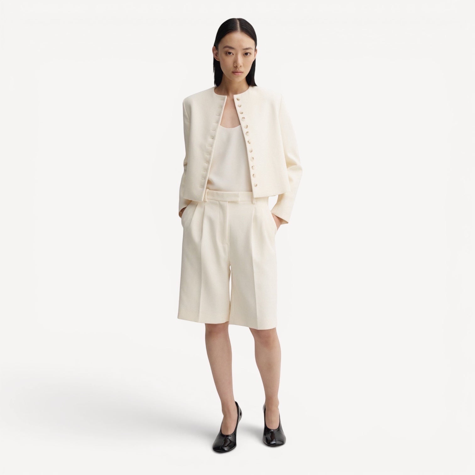 Lula Studio Prague cream woven blend shorts with front pleats and adjustable side tabs, worn by a model.